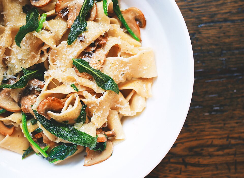 Sfeerfoto van pasta met kaas, kruiden en paddenstoelen op een bord