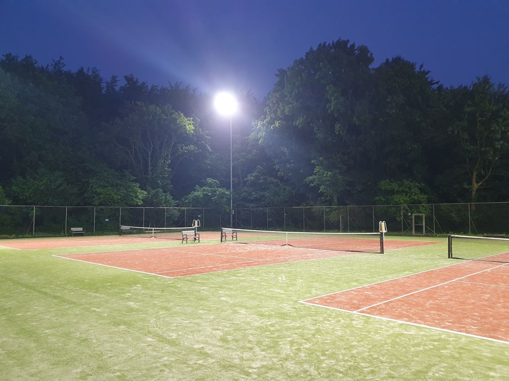 Sfeerfoto van verlichte tennisbanen in de avond
